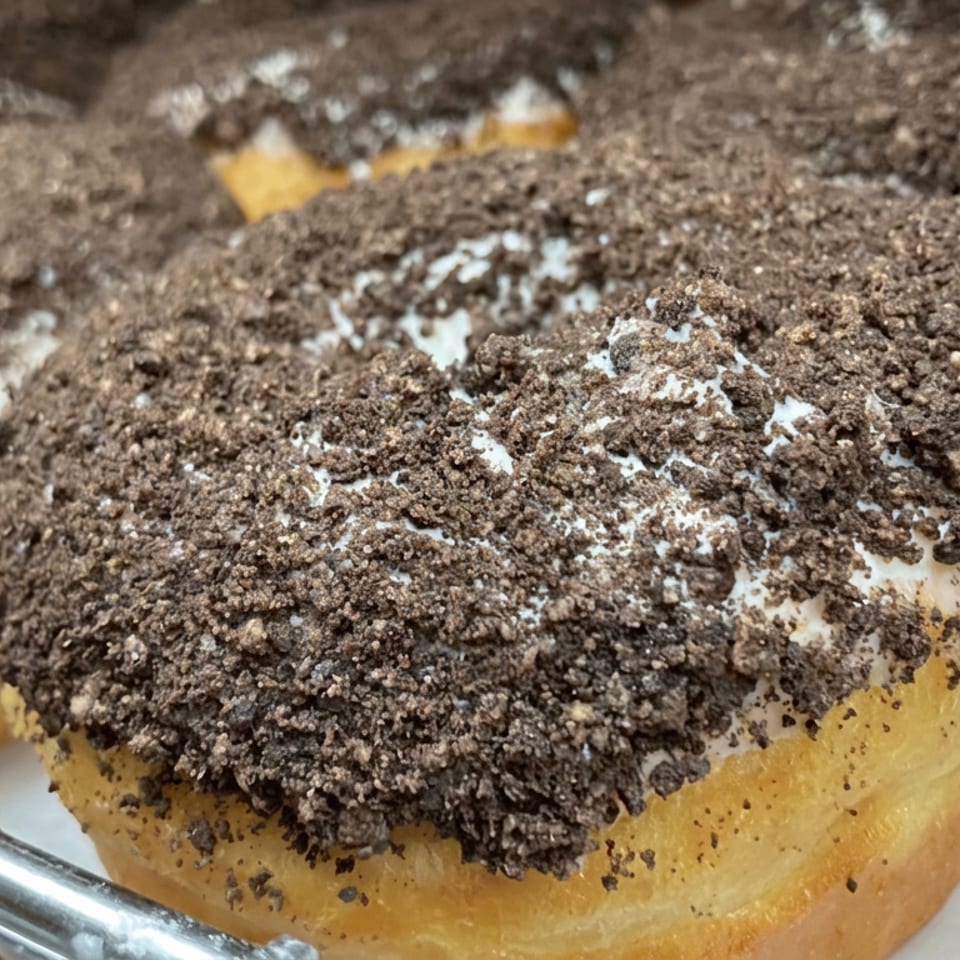 Close-up of golden pastries topped with white cream and a generous layer of chocolate cookie crumbs on a serving tray.